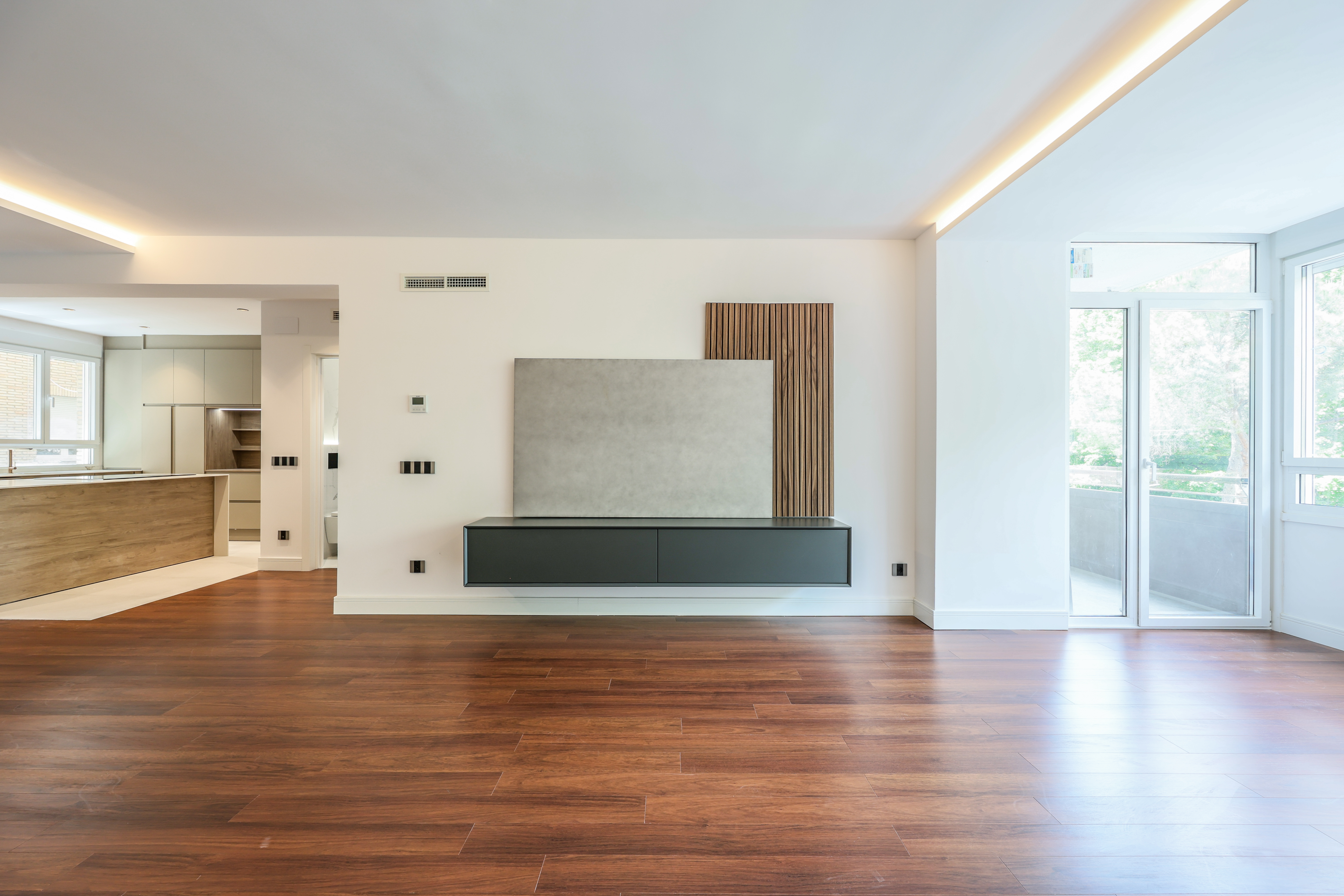 Salón vacío con suelo de tarima oscura y mueble de televisión flotante