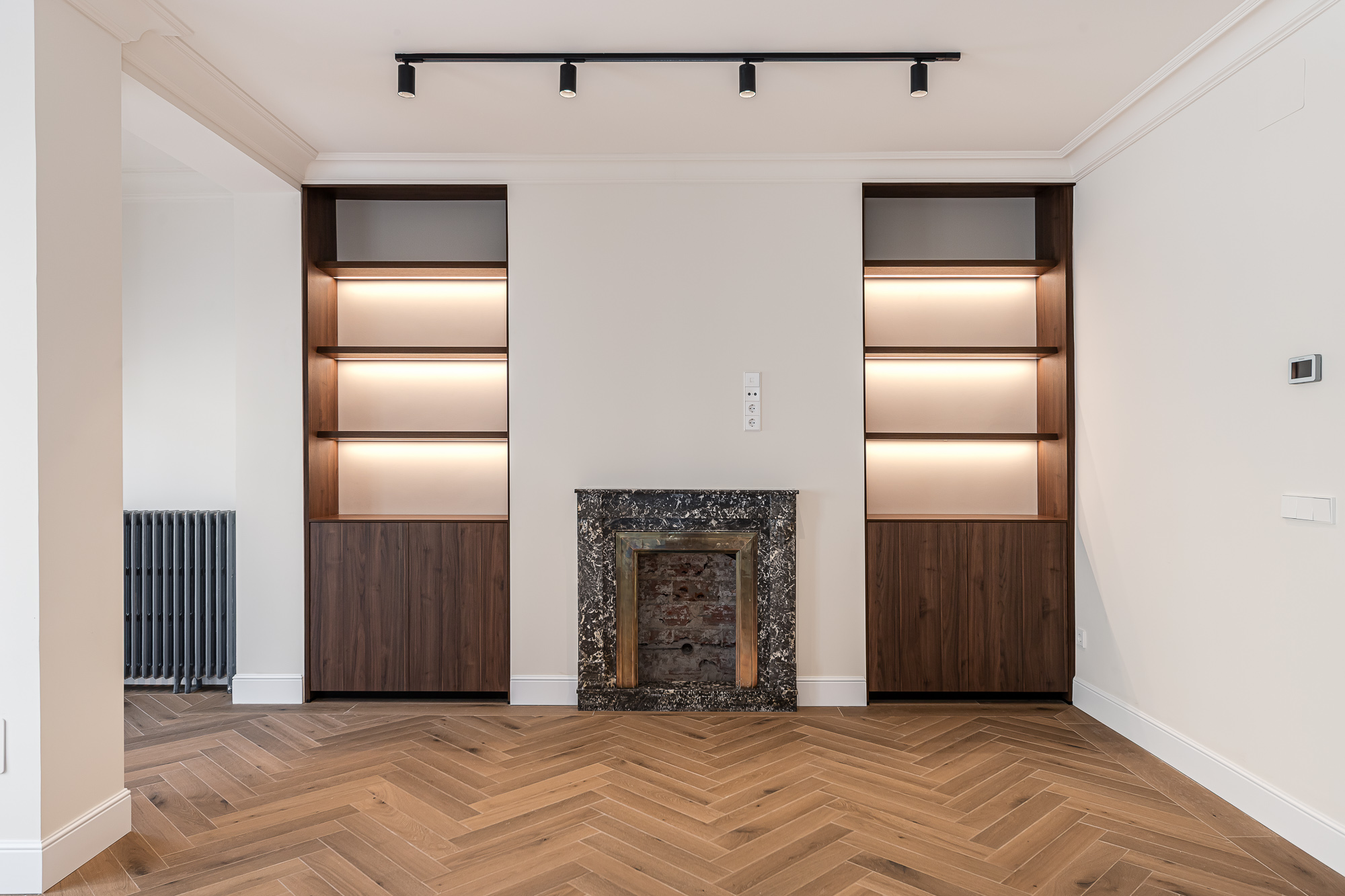 Salón con suelo de madera en espiga, estanterías de madera empotradas con iluminación integrada y chimenea con marco de piedra oscura — Vivienda Lucio del Valle