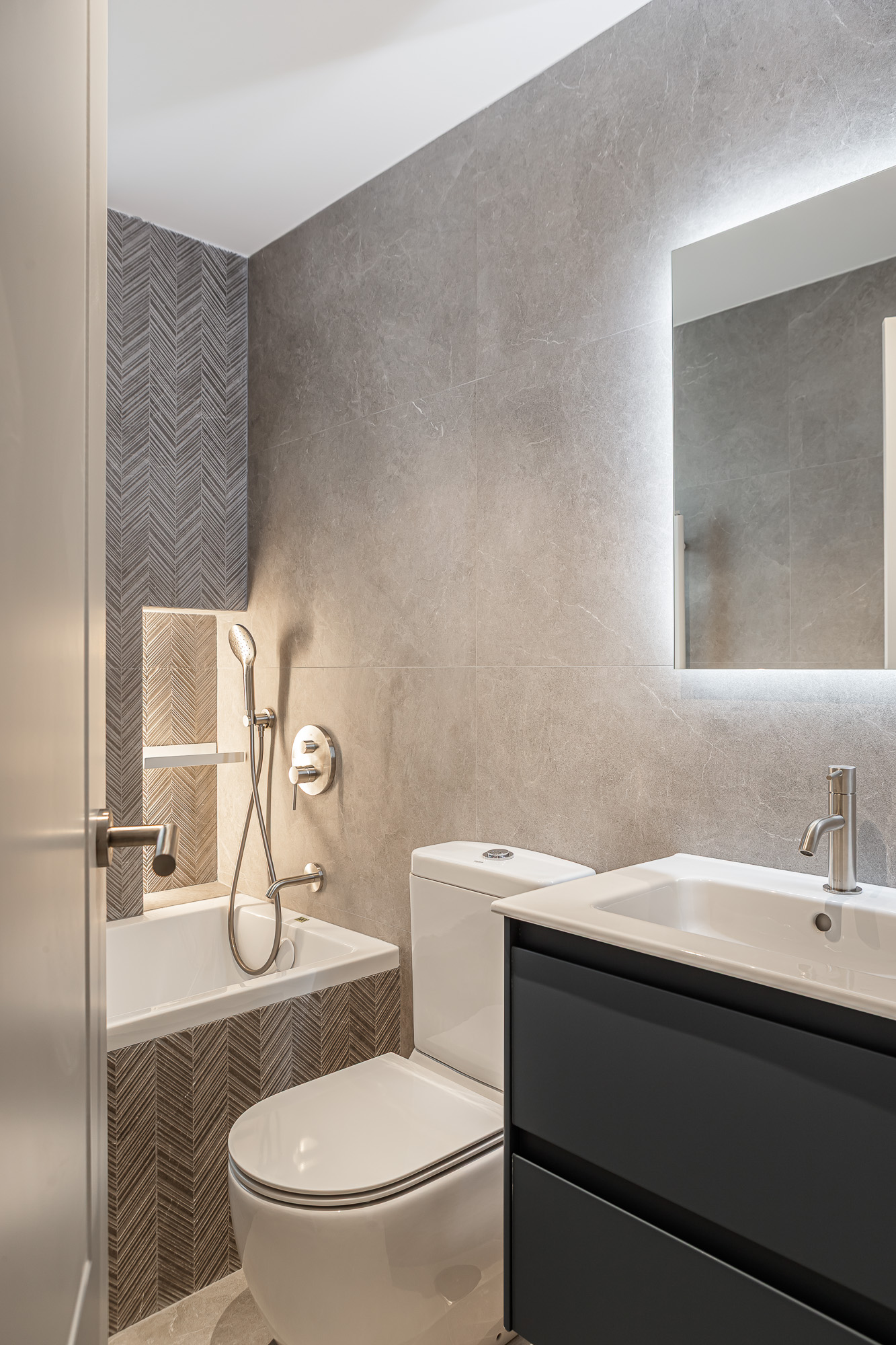Baño con bañera, hornacina con revestimiento en espiga, inodoro y espejo retroiluminado
