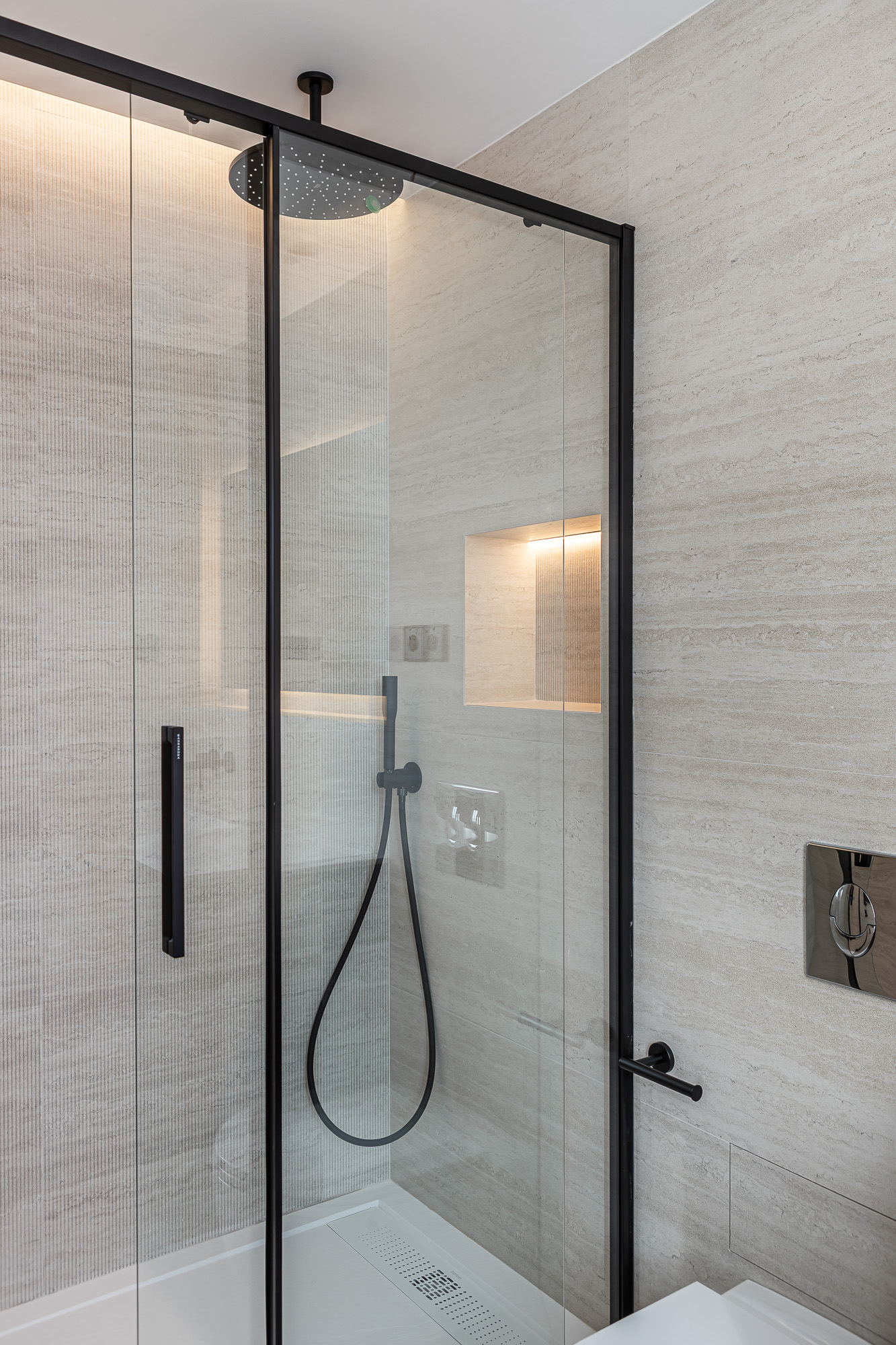 Ducha de obra con mampara de cristal y perfilería negra, ducha de lluvia y hornacina iluminada