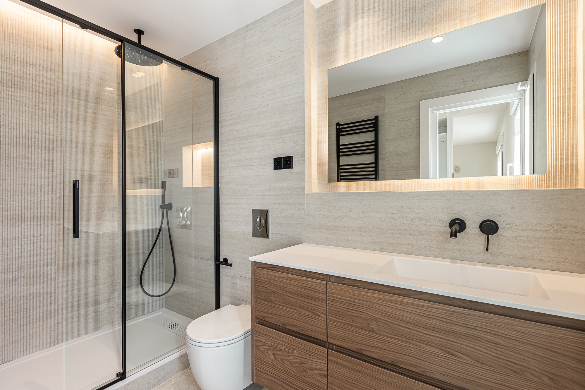 Baño con mampara de cristal con perfilería negra, mueble de madera y espejo retroiluminado