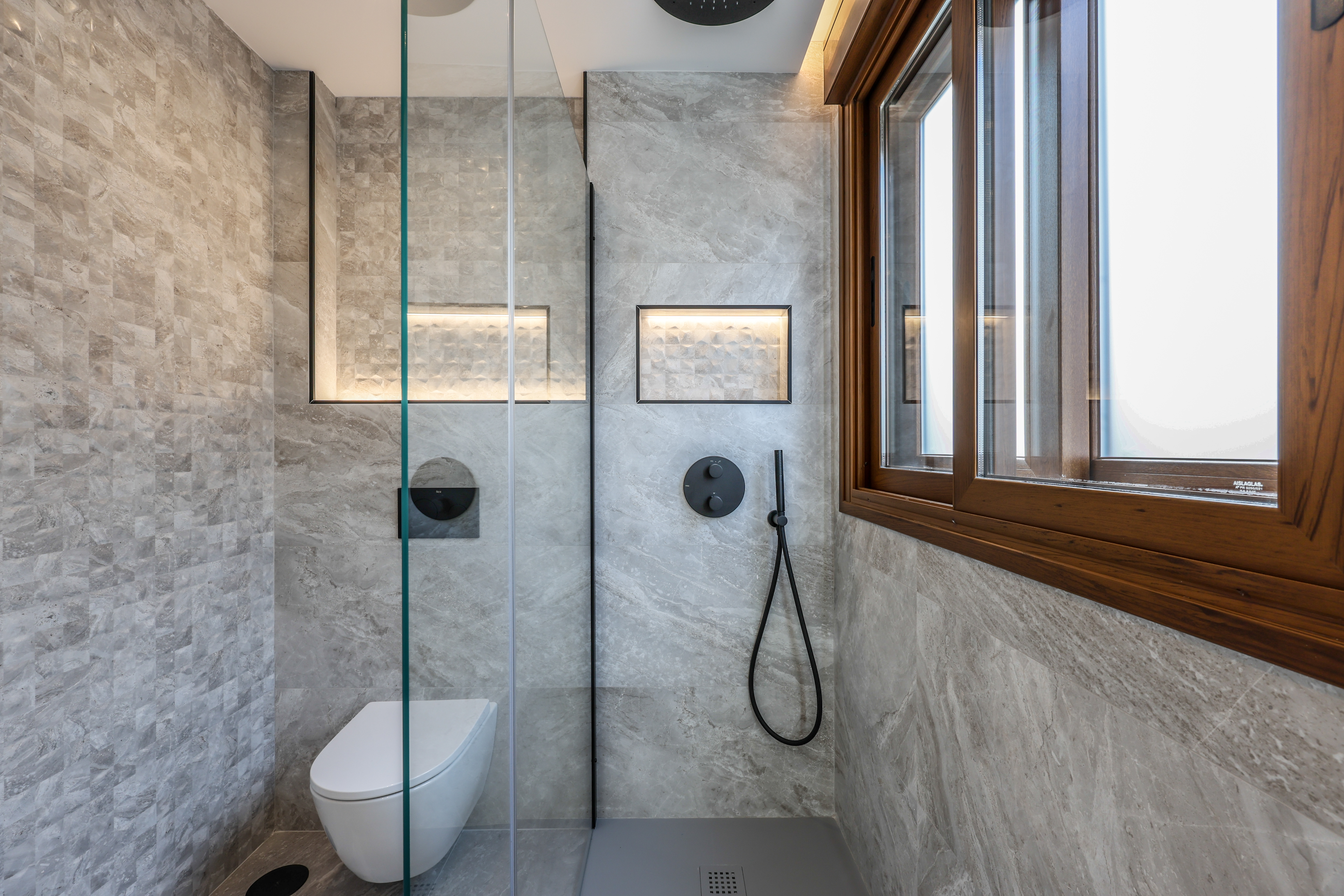 Ducha de obra con nicho iluminado y grifería negra, mármol gris