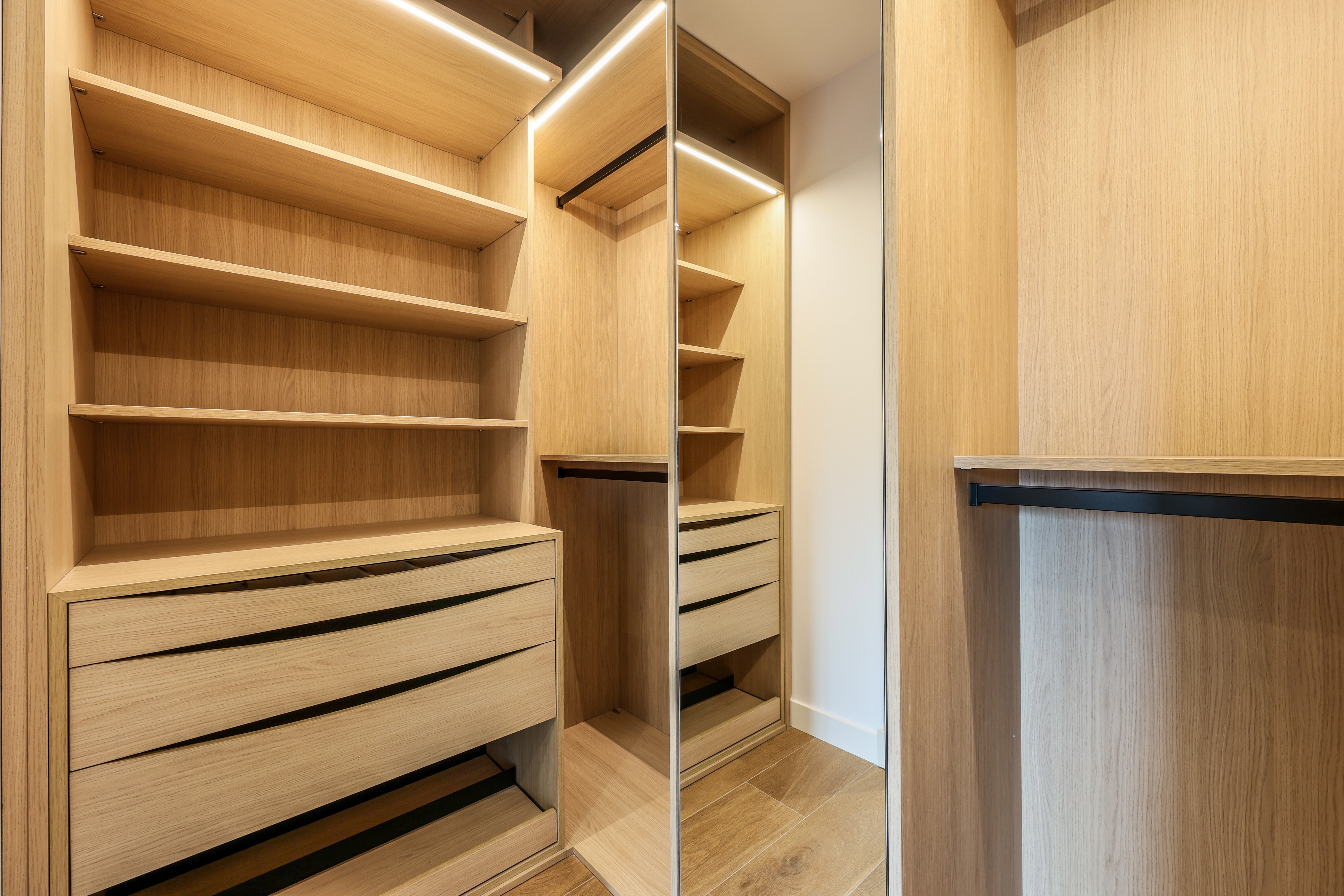 Vestidor con estanterías de madera clara, cajonera y espejo integrado