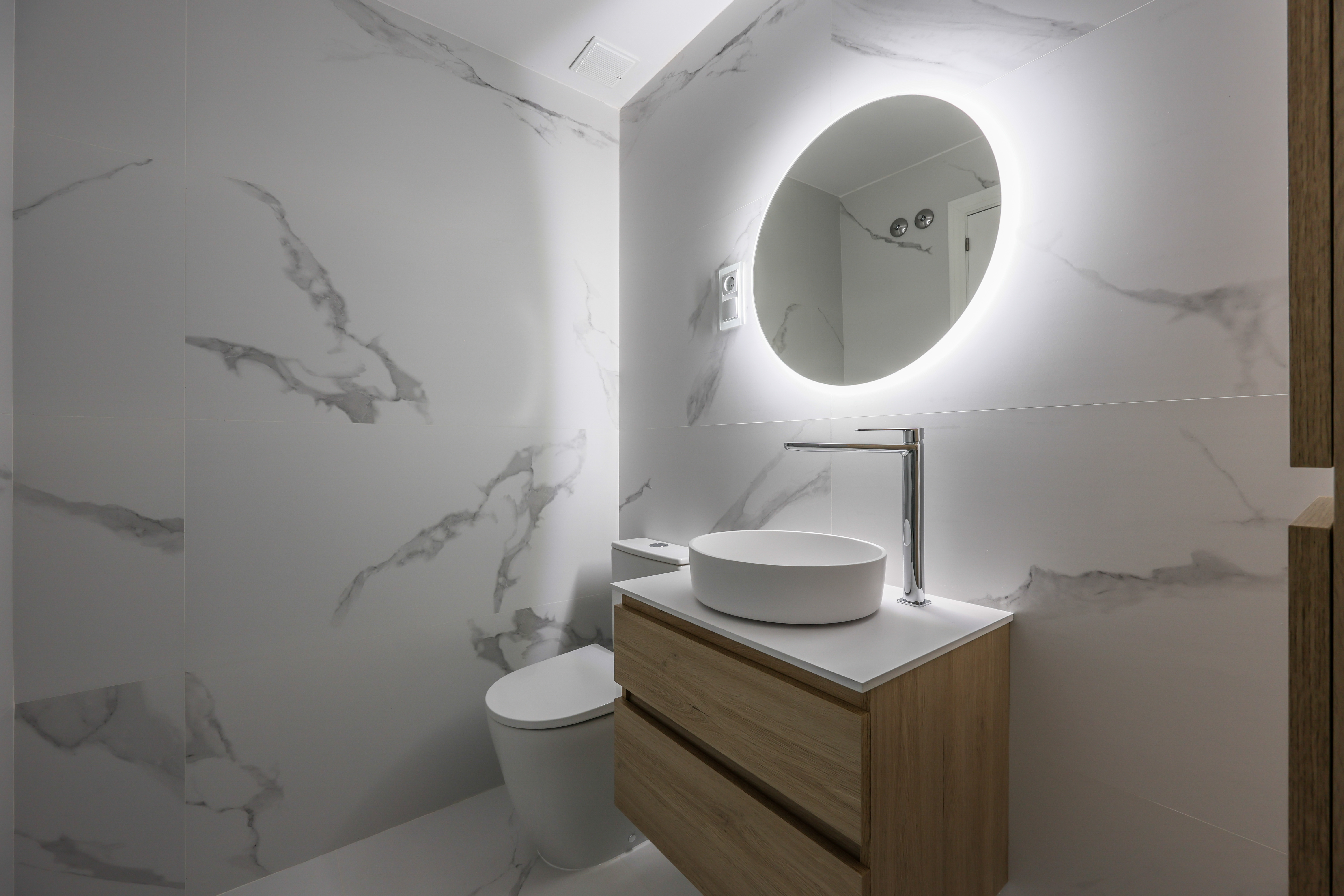 Aseo de mármol blanco con lavabo redondo sobre encimera de madera