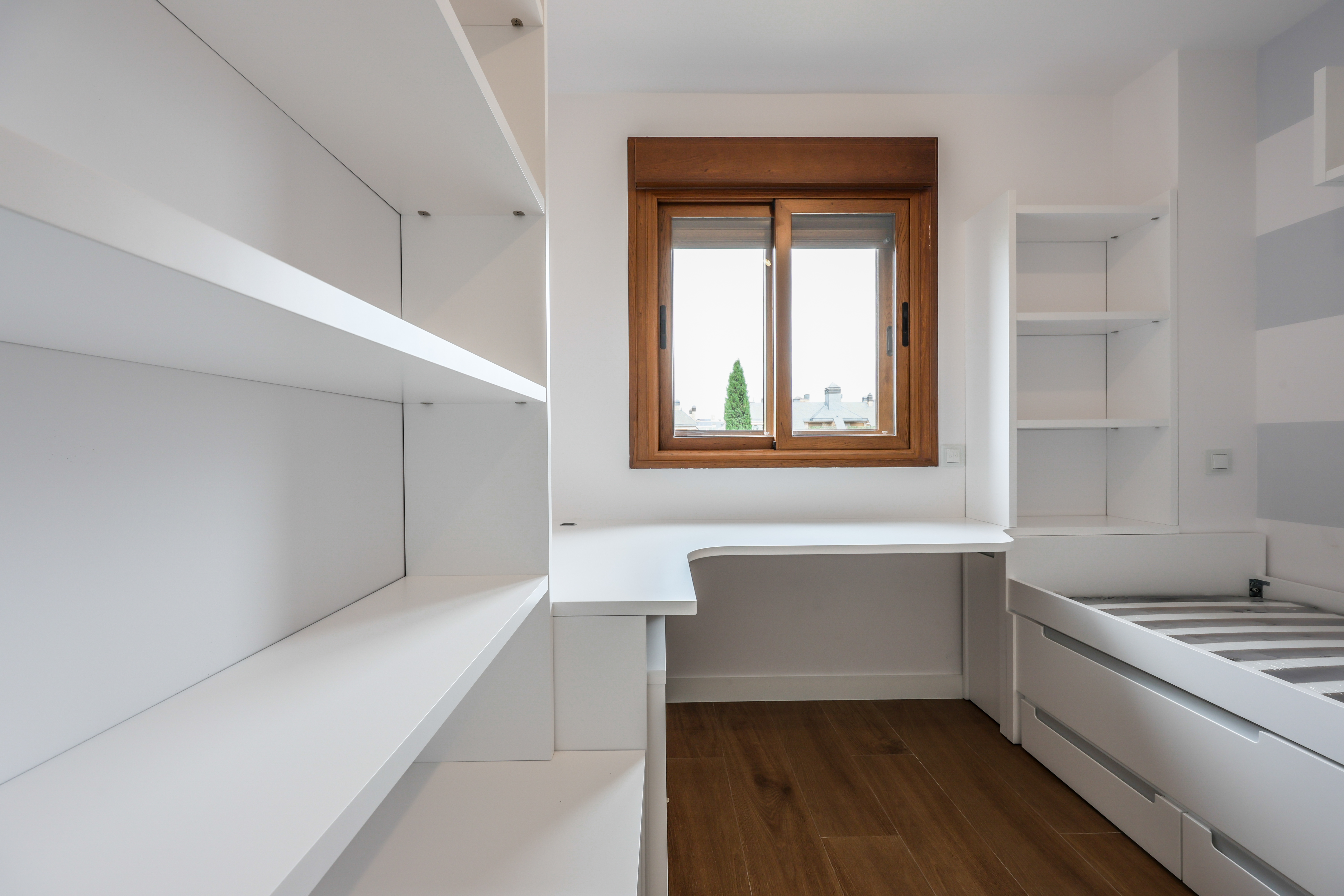 Habitación infantil con escritorio bajo ventana y mobiliario blanco