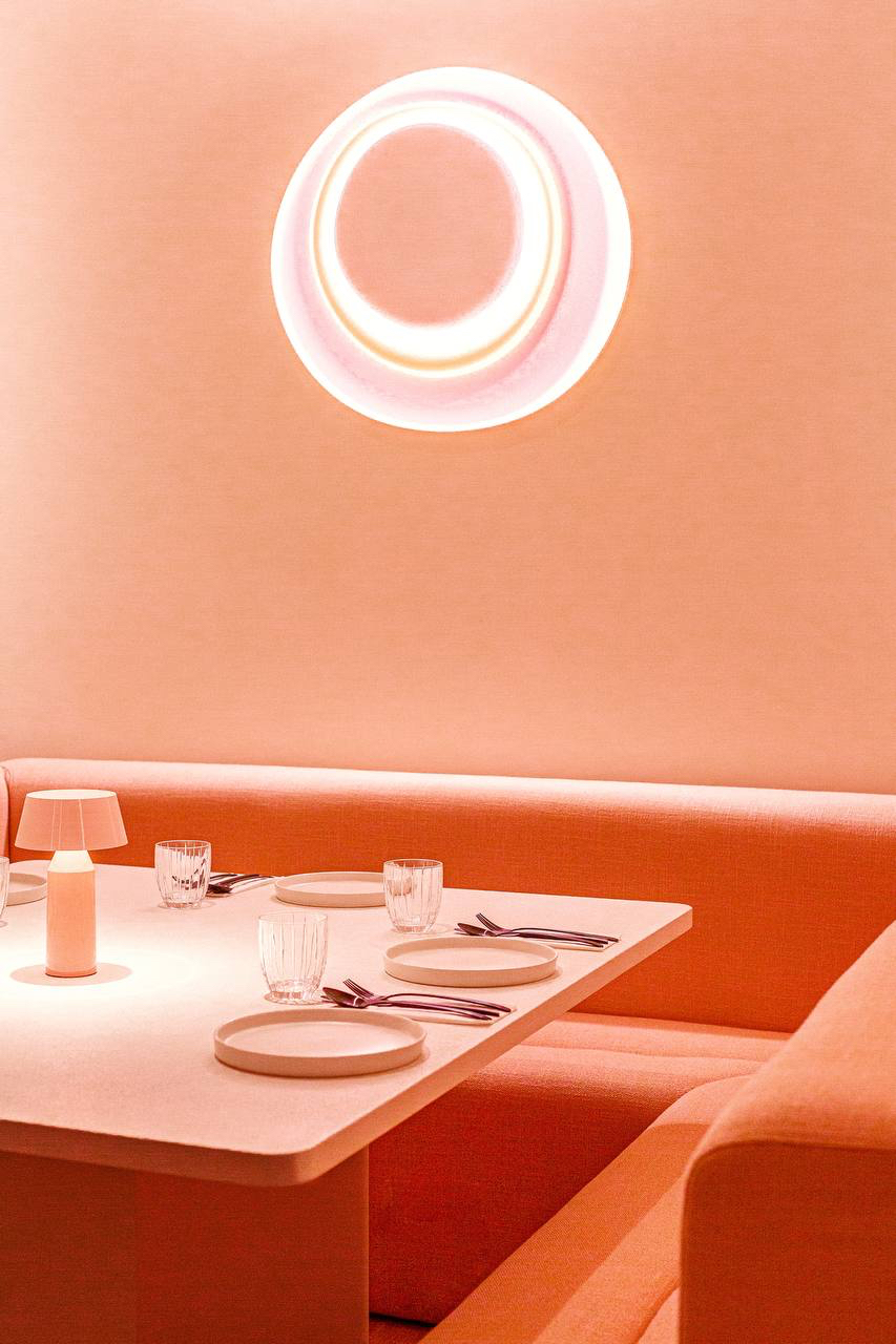Aplique circular luminoso sobre una banqueta naranja y una mesa puesta