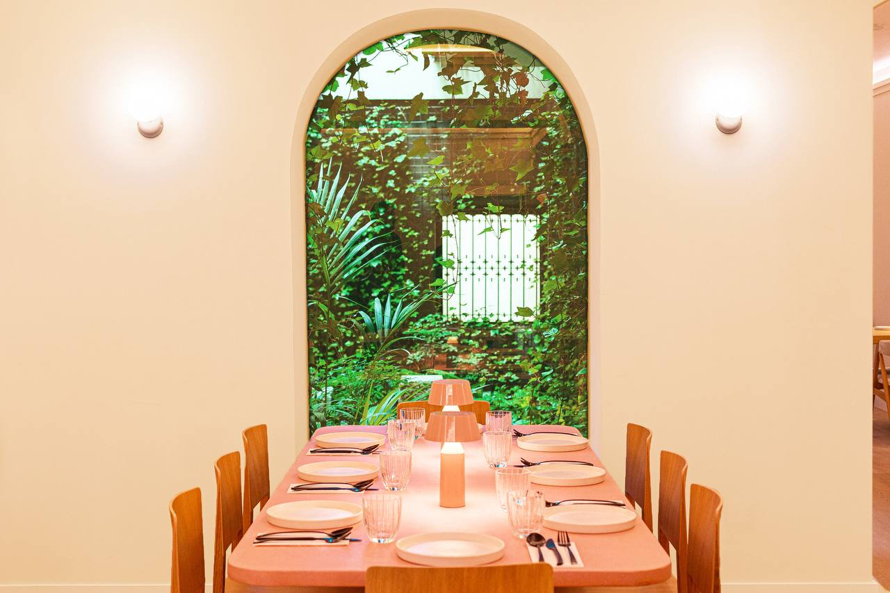 Mesa corrida frente a un arco que enmarca un patio interior cubierto de hiedra — Restaurante Mudrá