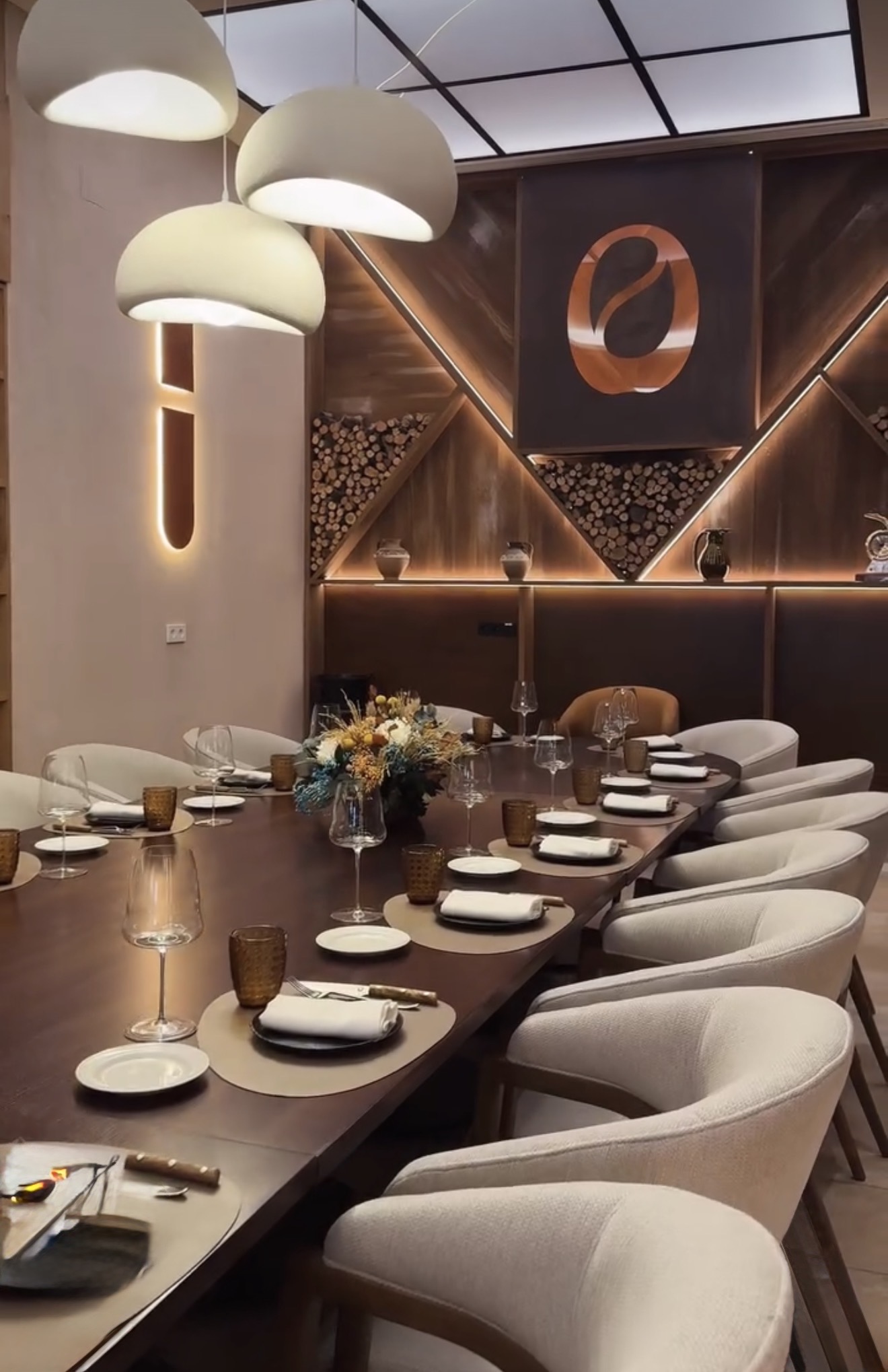 Detalle de la mesa puesta con copas, vasos ámbar y flores secas, con la pared de madera iluminada al fondo