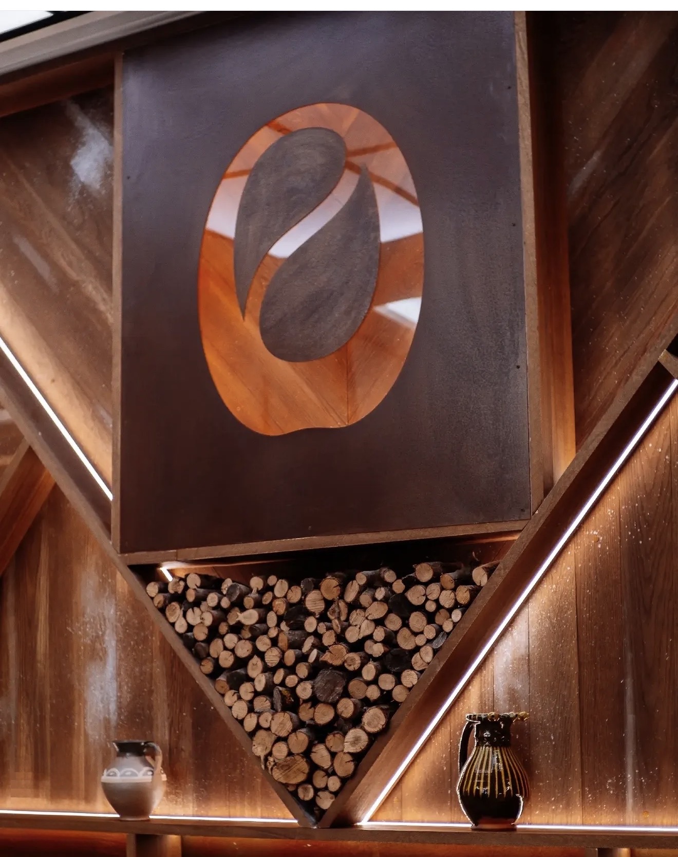 Detalle de un panel con emblema ovalado recortado y un nicho triangular con leña apilada, entre líneas de luz